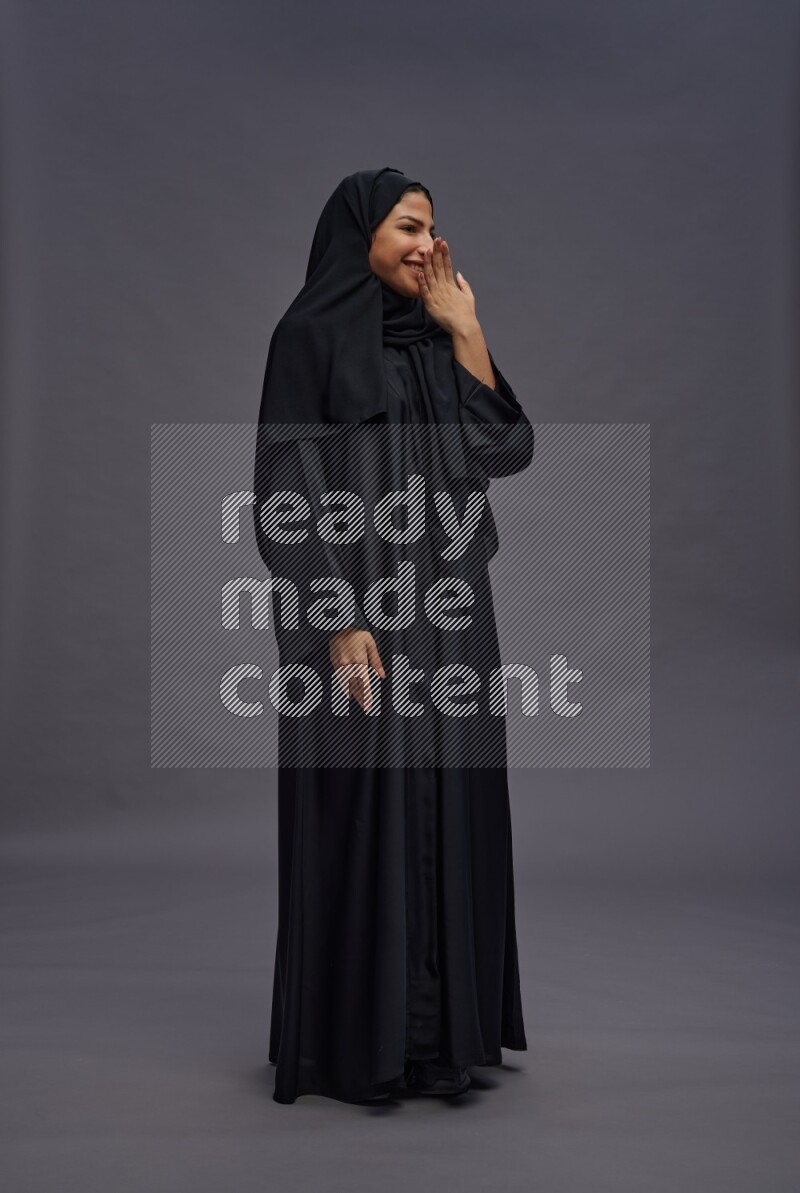 Saudi woman wearing Abaya standing interacting with the camera on gray background