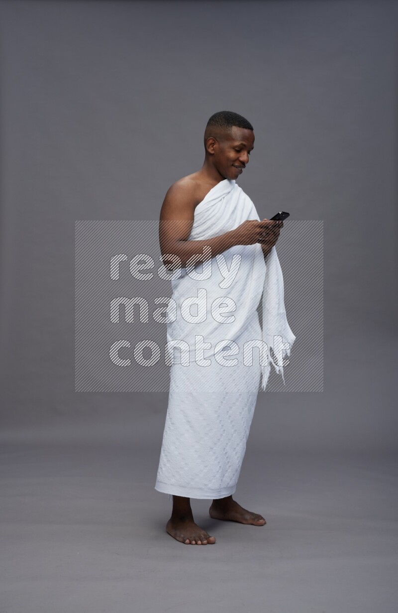 A man wearing Ehram Standing texting on phone on gray background
