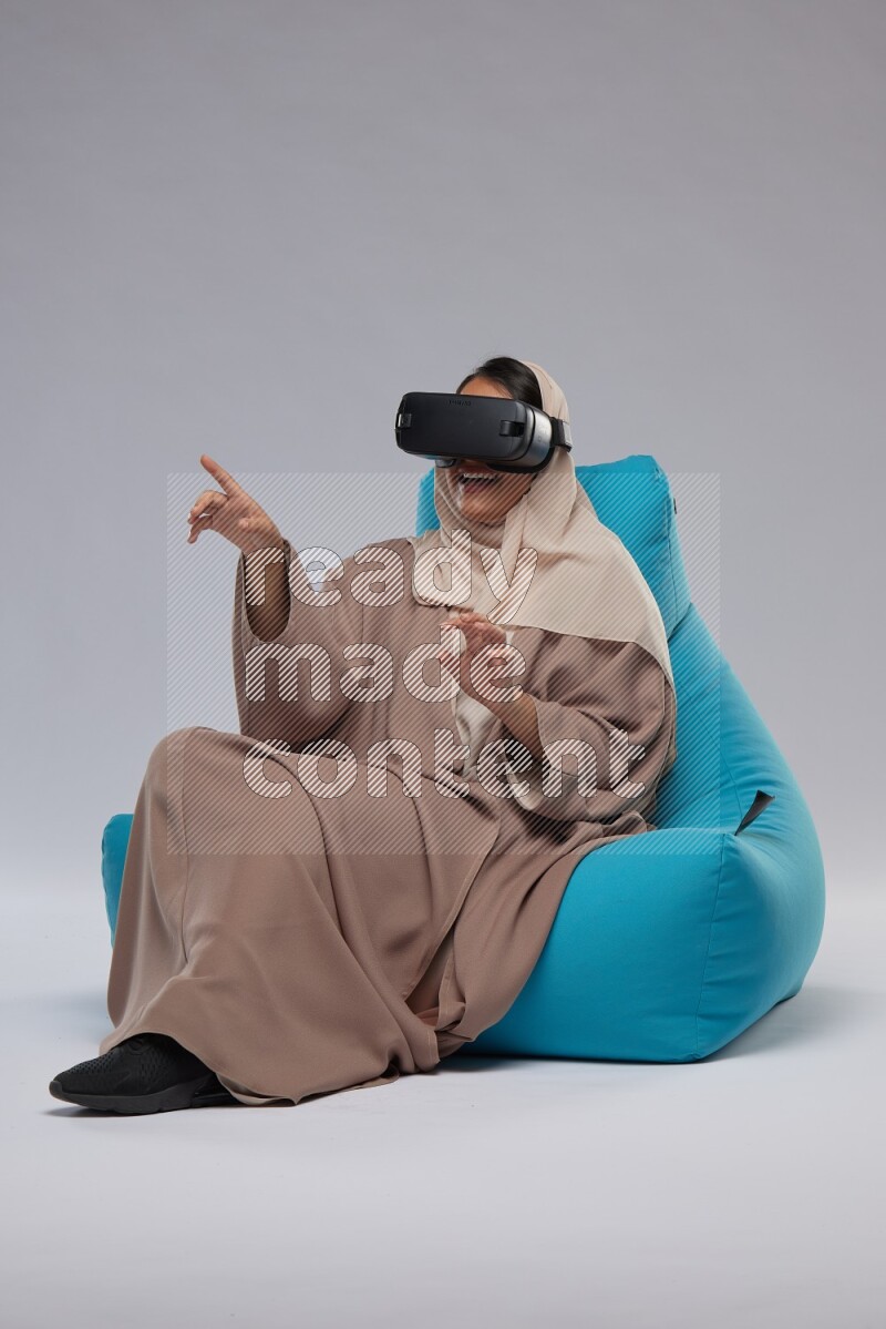A Saudi woman sitting on a blue beanbag and gaming with VR