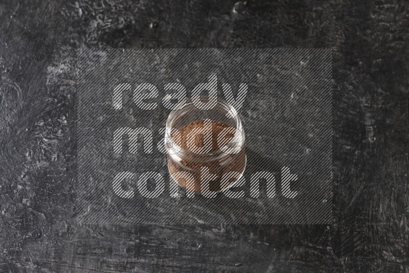 A glass jar full of cloves powder on a textured black flooring
