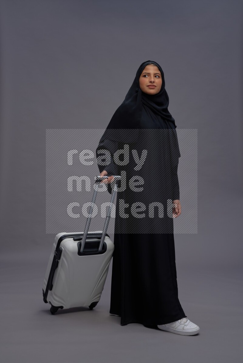 Saudi woman wearing Abaya standing holding bag on gray background