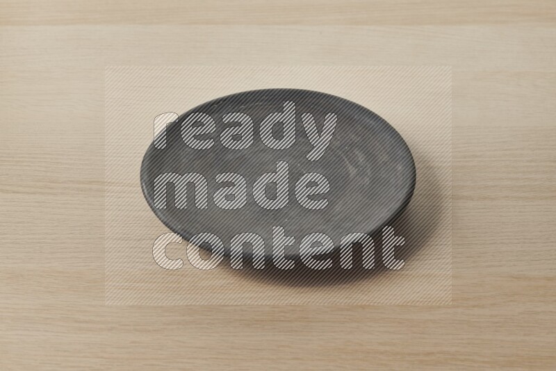 A circular black pottery plate on light wooden background