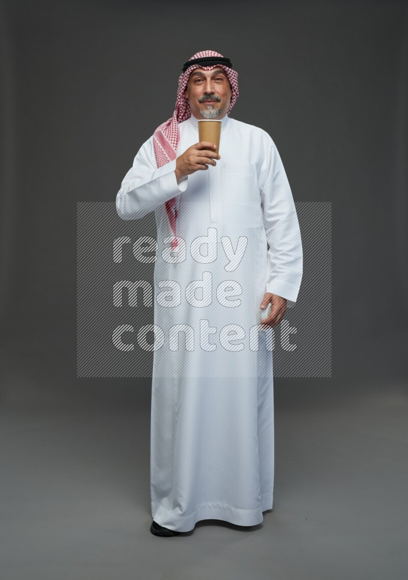 Saudi man with shomag Standing holding paper cup on gray background