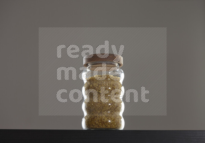 Coarse bulgur in a glass jar on black background