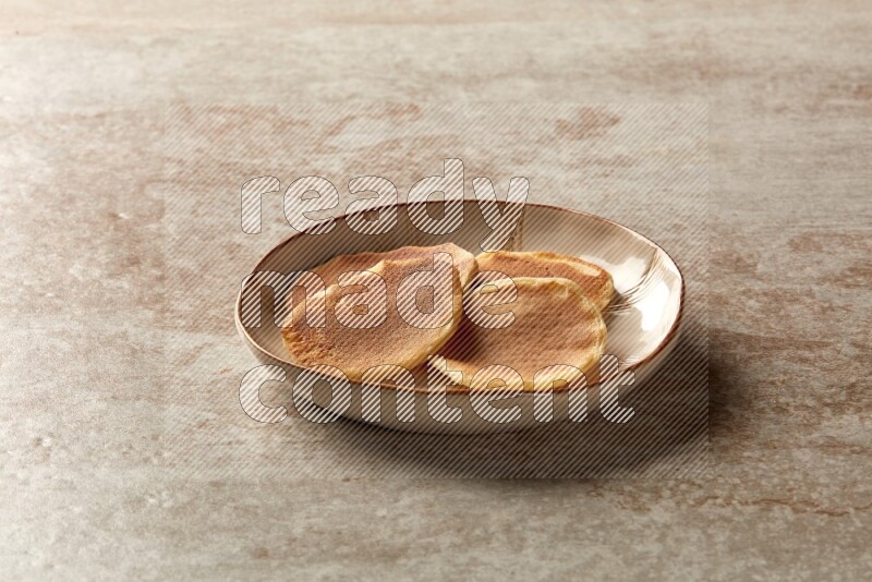 Four stacked plain mini pancakes in an irregular plate on beige background
