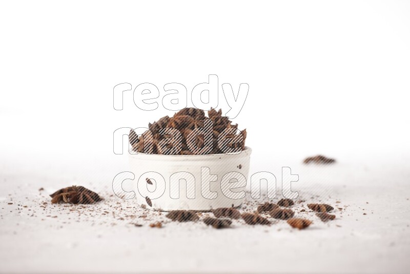 Star Anise in a white bowl and more of it sprinkled on white background