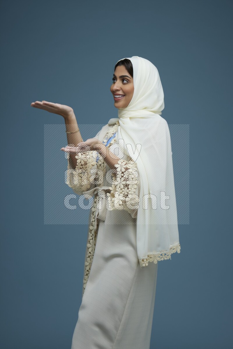 A Saudi woman pointing in a blue background wearing an off-white Abaya Hijab