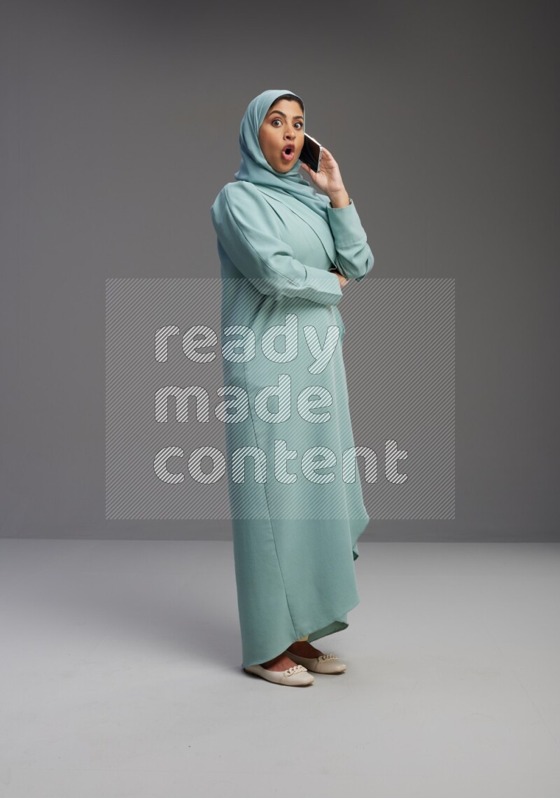 Saudi Woman wearing Abaya standing talking on phone on Gray background
