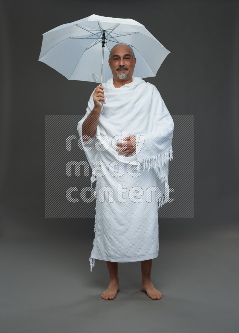 A man wearing Ehram Standing holding umbrella on gray background