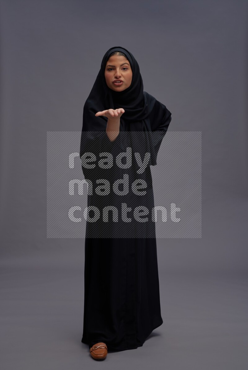 Saudi woman wearing Abaya standing interacting with the camera on gray background