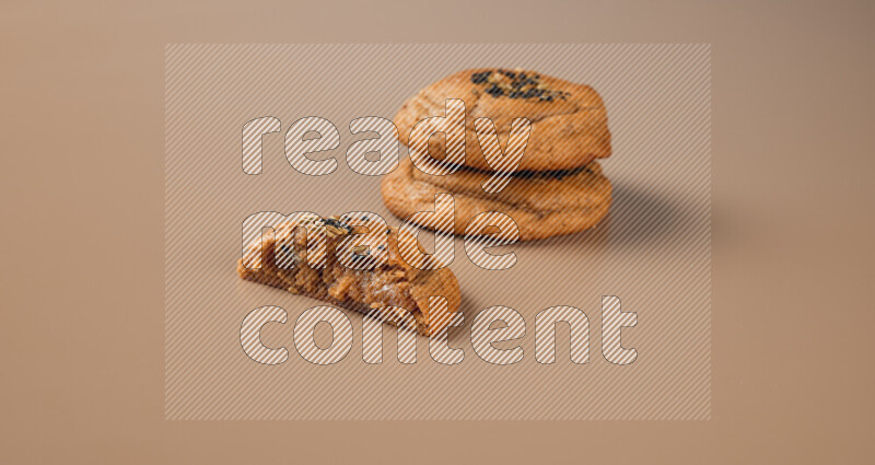 Two Hasawi cookies field of date and decorated by black seed and anise grain with another one cut in half on a brown background