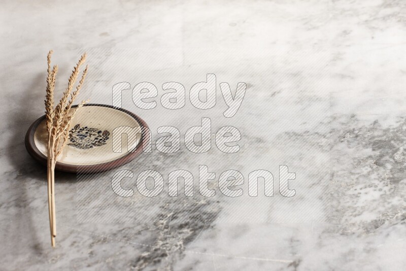 Wheat stalks on decorative pottery plate on grey marble background