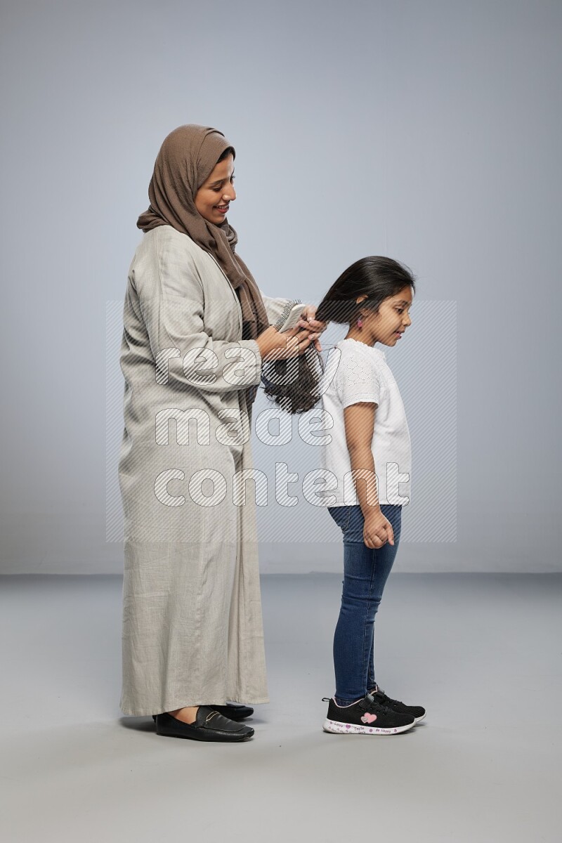 Mom standing styling hair for her daughter on gray background