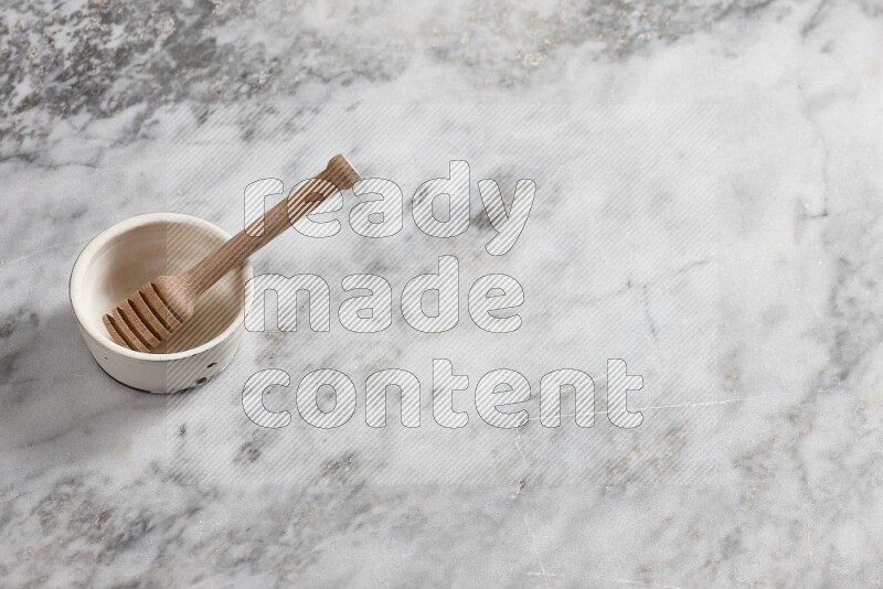 White pottery bowl with wooden honey dipper in it on grey marble background