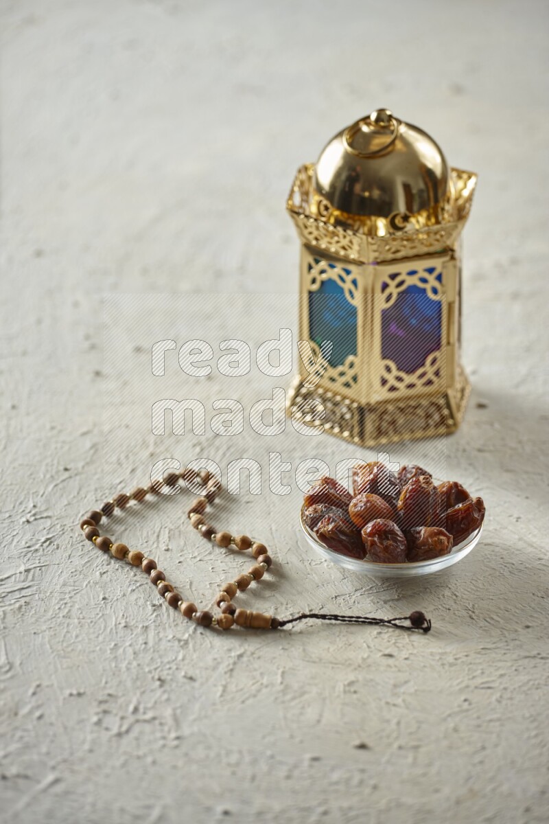 A golden lantern with different drinks, dates, nuts, prayer beads and quran on textured white background