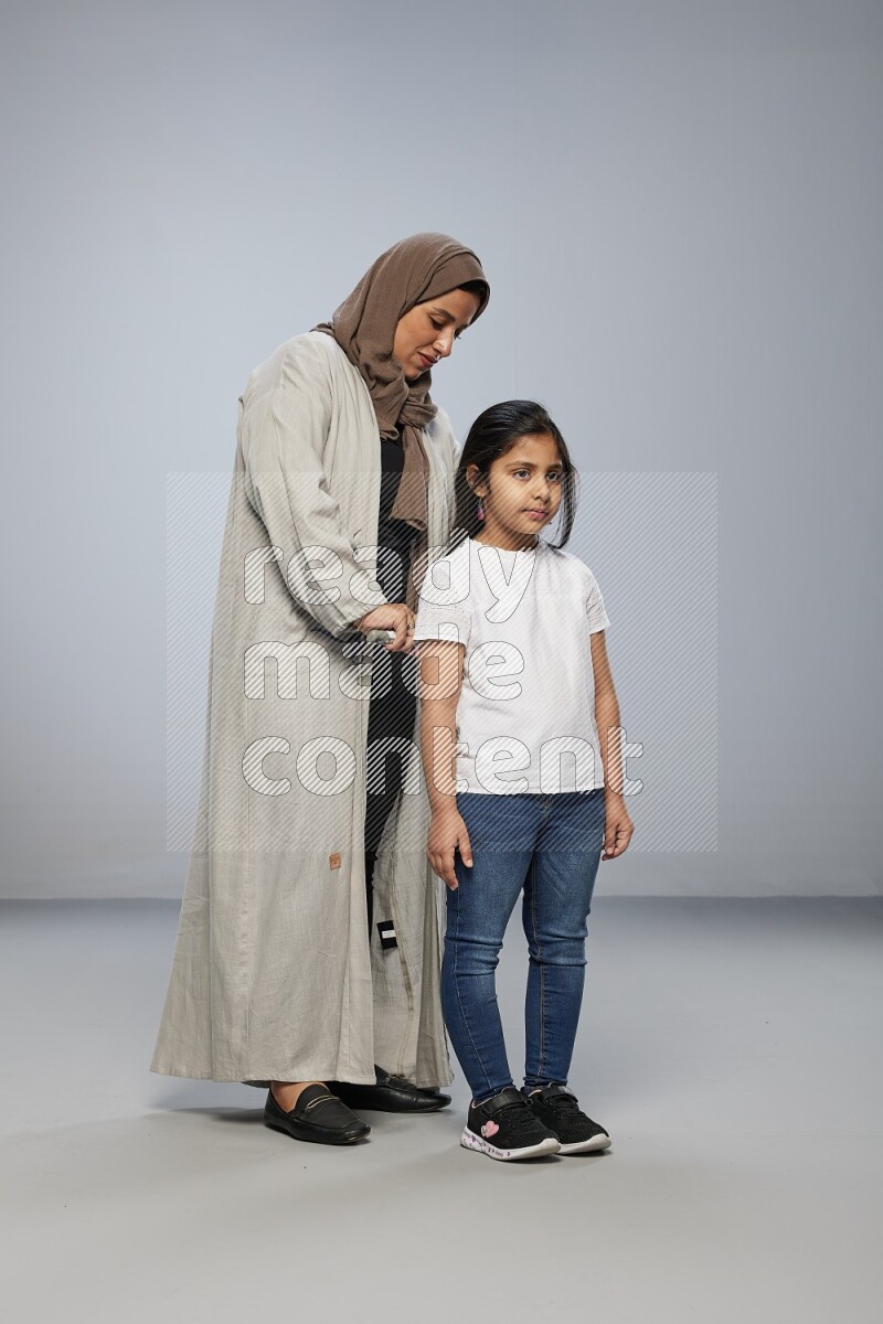 Mom standing styling hair for her daughter on gray background