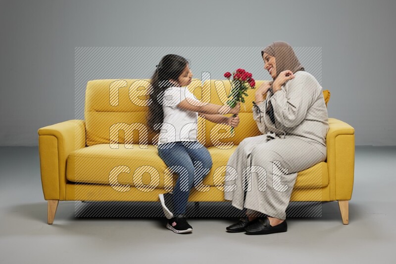 A girl sitting giving flowers to her mother on gray background