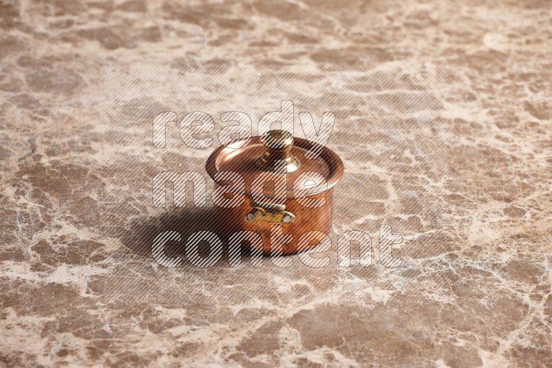 A small copper pot on beige marble background