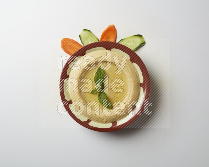 Hummus in a traditional plate garnished with mint on a white background