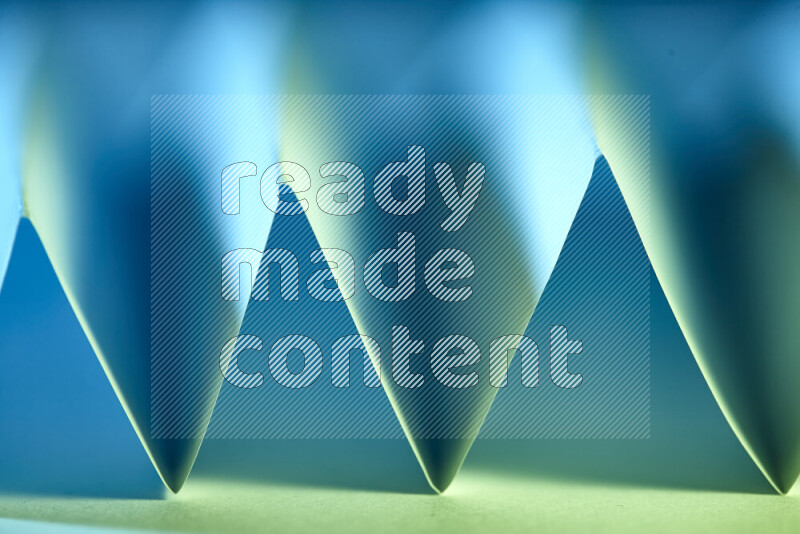 A close-up abstract image showing sharp geometric paper folds in green and blue gradients