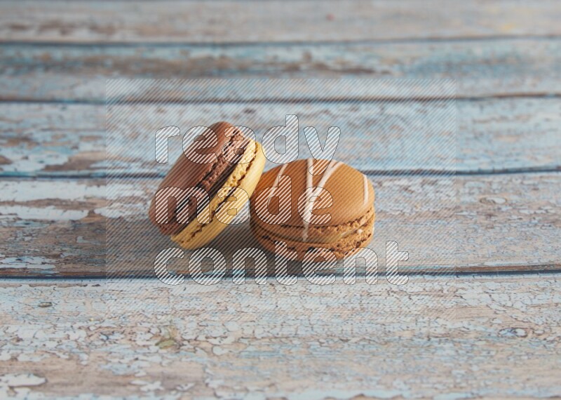 45º Shot of of two assorted Brown Irish Cream, and Yellow, and Brown Chai Latte macarons  on light blue background