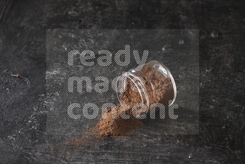 A flipped glass jar full of cloves powder on a textured black flooring