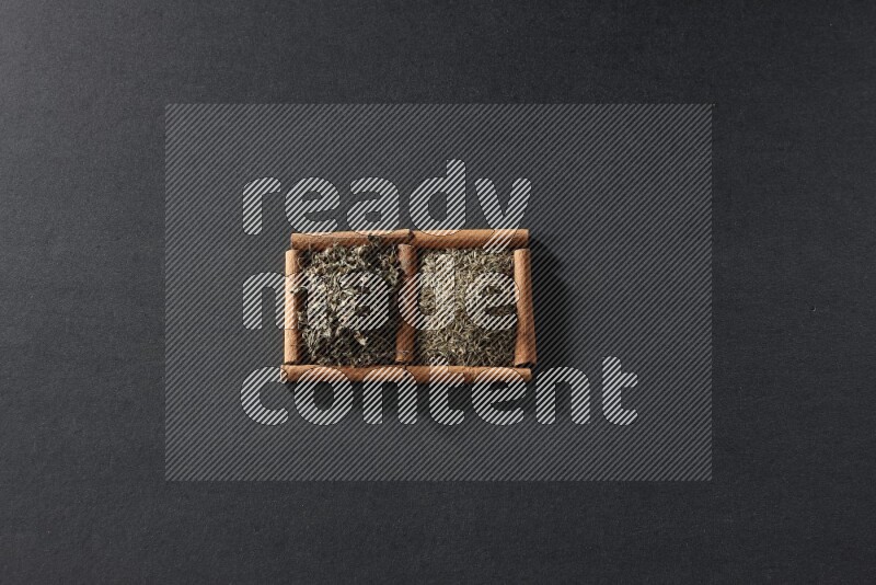 مربعان من أعواد القرفة ممتلئان بحبوب الكمون والريحان المجفف علي خلفية سوداء