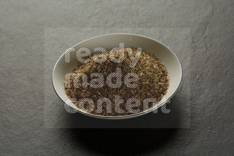 white ceramic round sauce dish filled with herbs on grey textured countertop