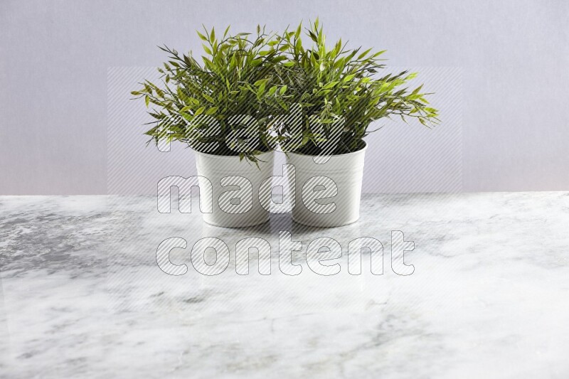 Two green artificial plants in white pot on grey marble background
