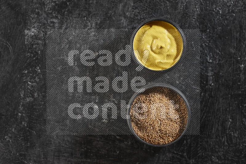 2 black pottery bowls full of mustard seeds and mustard paste on black flooring