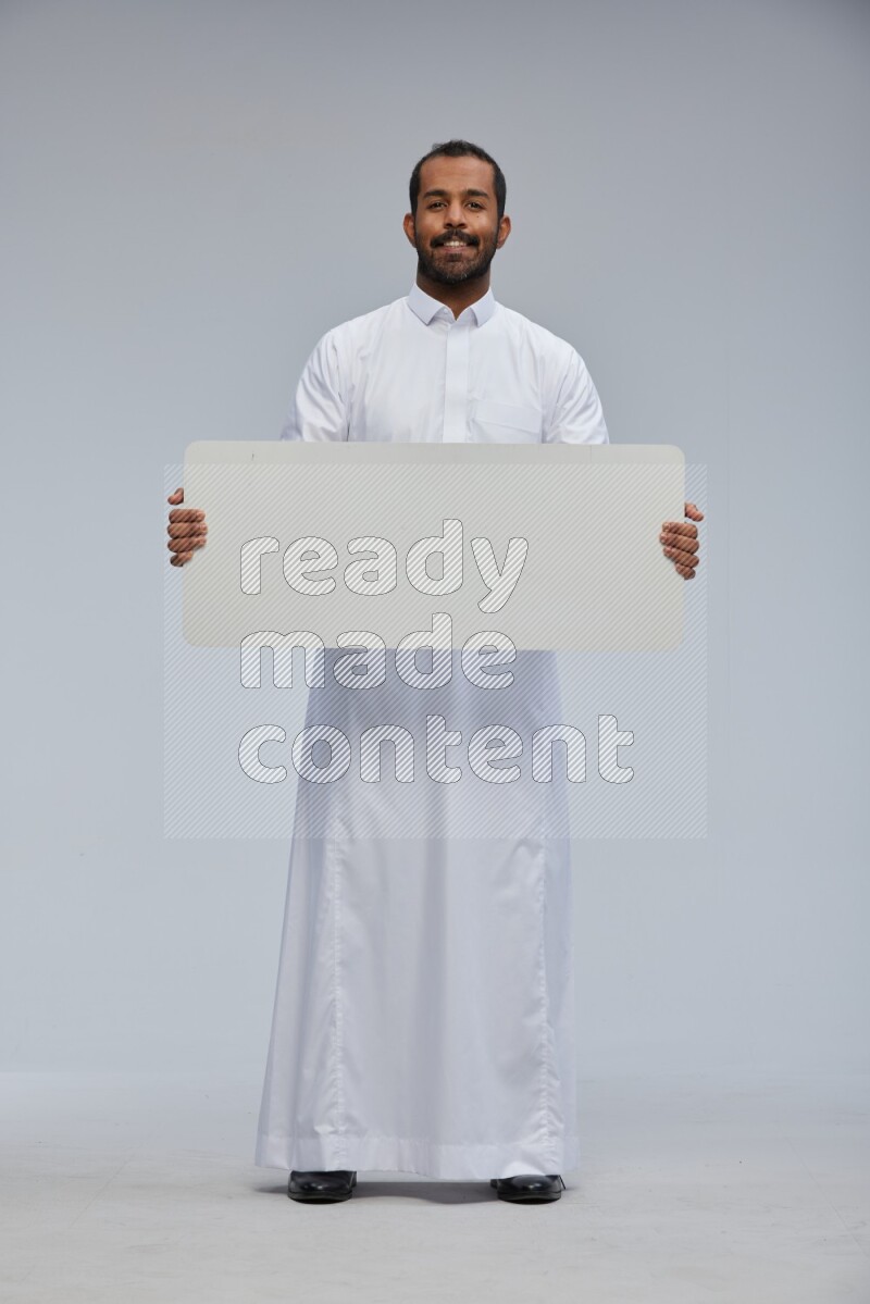 Saudi man wearing Thob standing holding board on Gray background