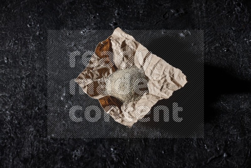 White pepper powder in a crumpled paper on textured black flooring