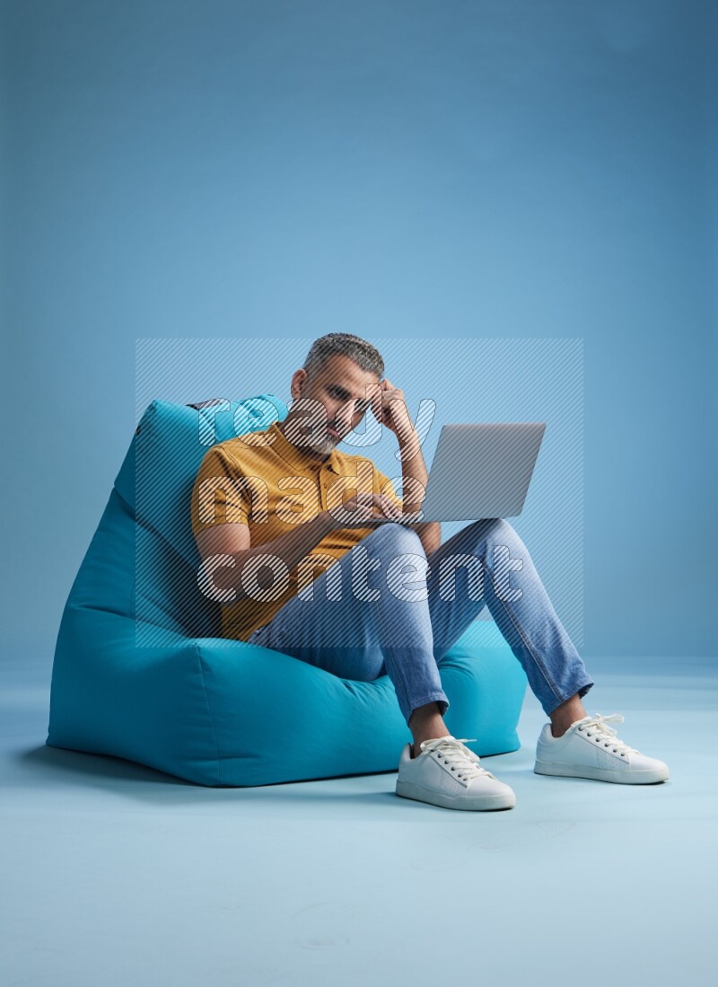 A man sitting on a blue beanbag and working on laptop
