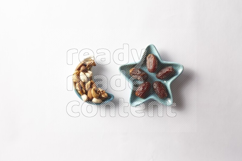 Dates in a star shaped pottery plate and a crescent plate with mixed nuts on white background