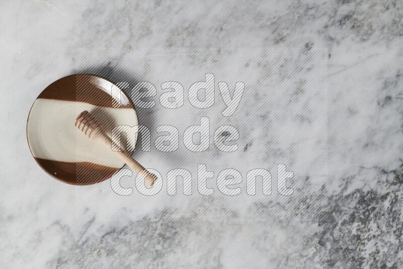 Multicolored pottery plate with wooden honey dipper in it on grey marble background