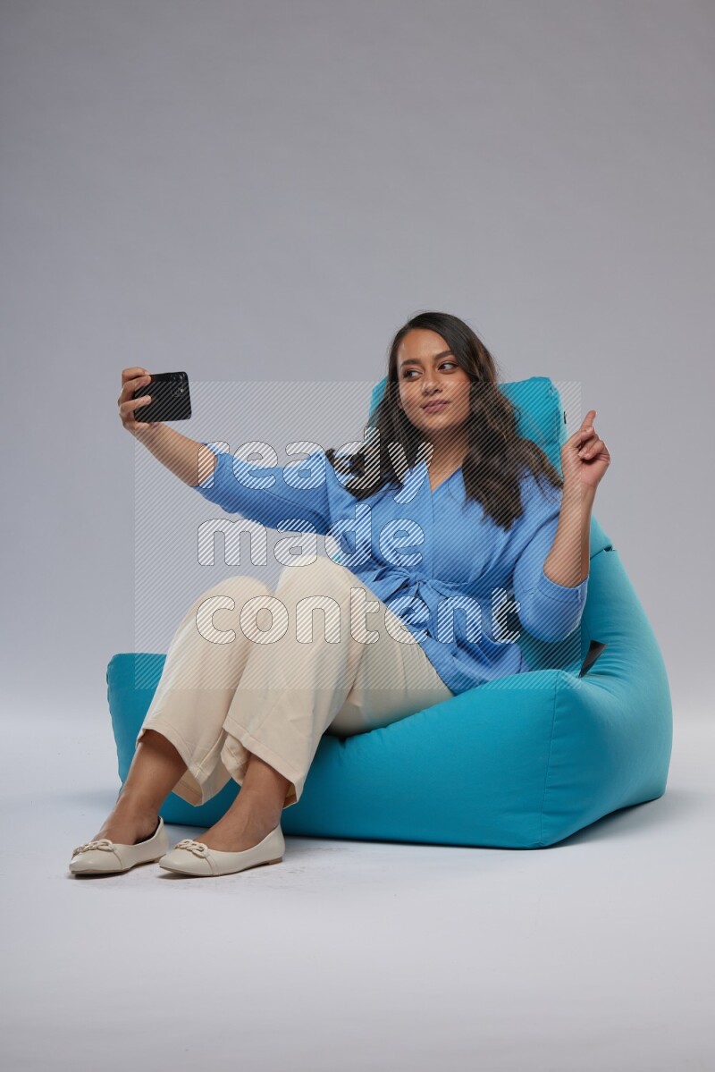 A woman sitting on a blue beanbag and taking selfie