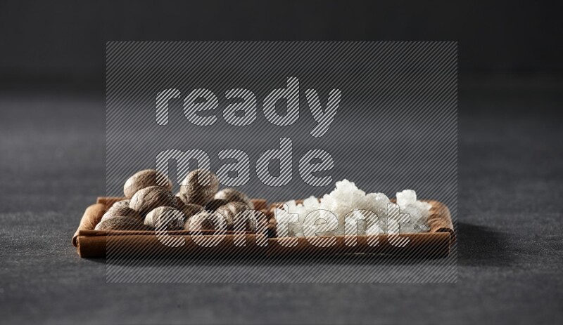 2 squares of cinnamon sticks full of nutmeg and white salt on black flooring