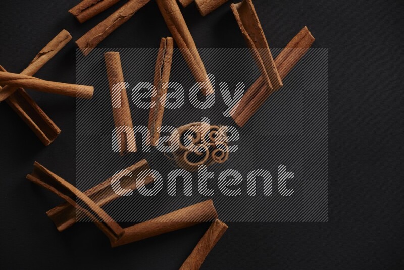 4 Cinnamon sticks stacked and bounded with more sticks in the background on black flooring