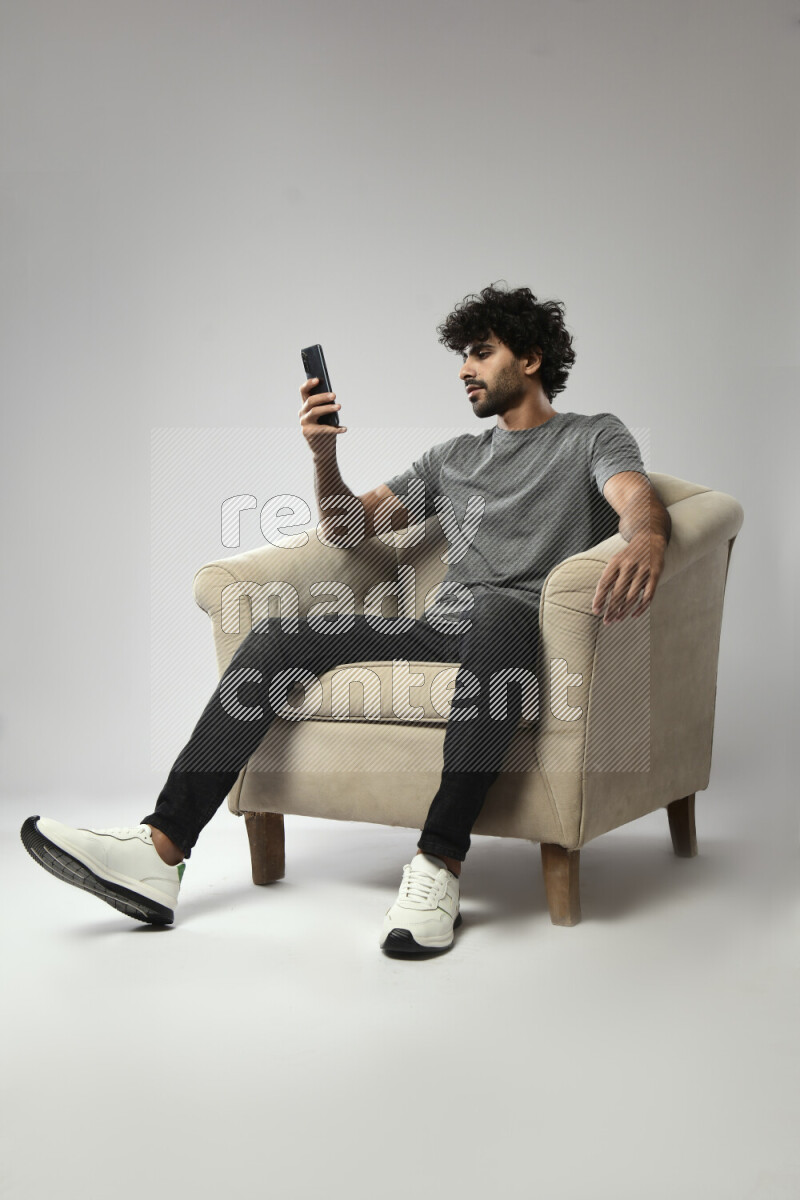 A man wearing casual sitting on a chair texting on the phone on white background