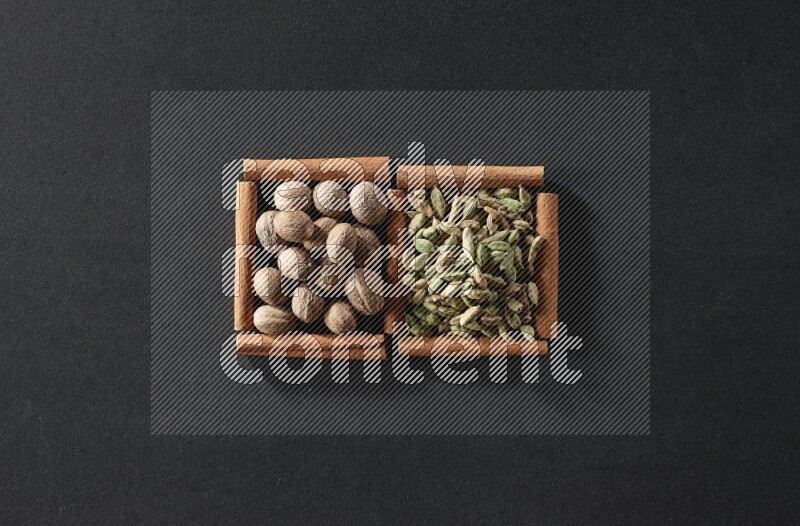 مربعان من أعواد القرفة ممتلئان بجوزة الطيب وحبوب الهيل علي خلفية سوداء