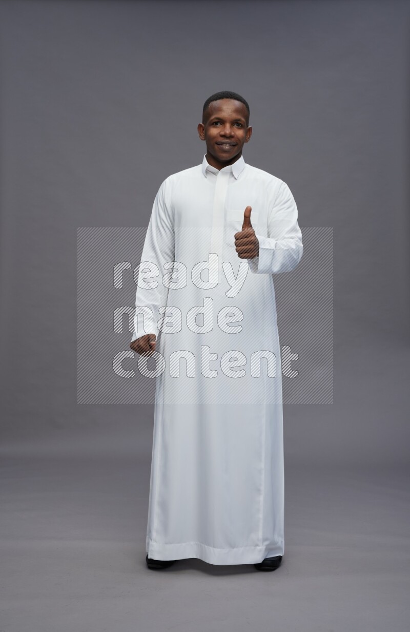 Saudi man wearing thob standing interacting with the camera on gray background