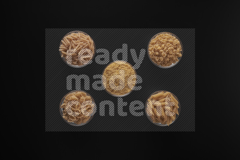 Different pasta types in 5 glass bowls on black background