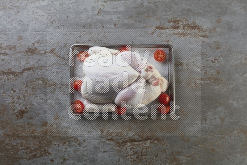 whole Raw chicken on a small oven trey direct on a rustic grey background