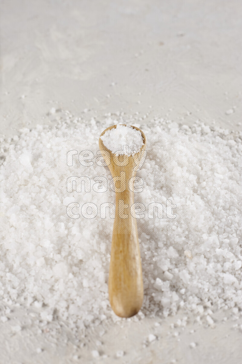 A wooden spoon full of white salt on white background