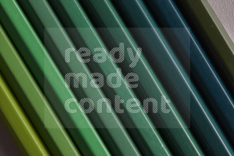 A collection of colored pencils arranged showcasing a gradient of green hues on grey background