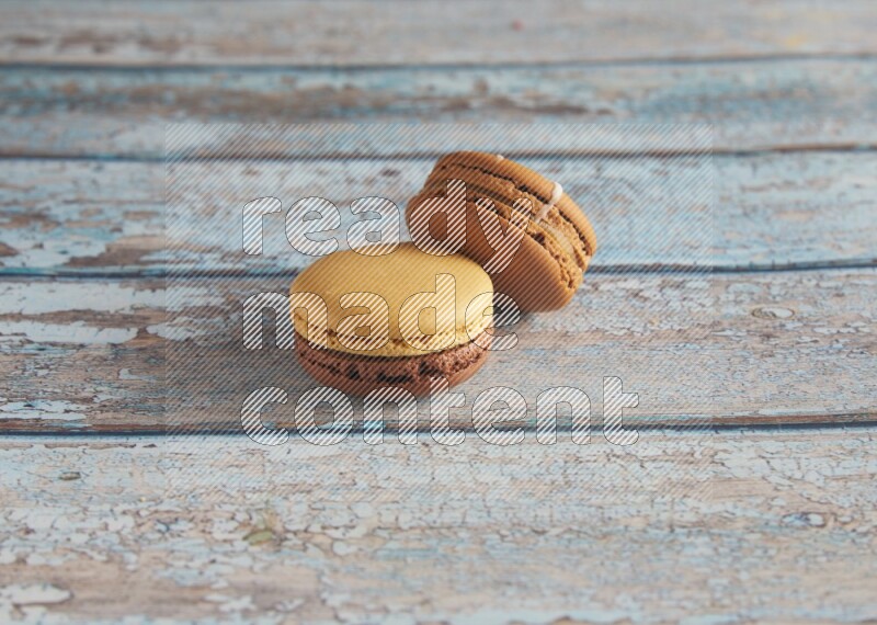 45º Shot of of two assorted Brown Irish Cream, and Yellow, and Brown Chai Latte macarons  on light blue background