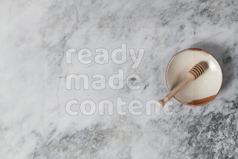 Multicolored pottery plate with wooden honey dipper in it on grey marble background