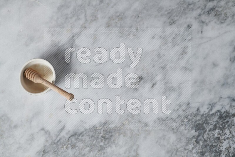 Beige pottery bowl with wooden honey dipper in it on grey marble background