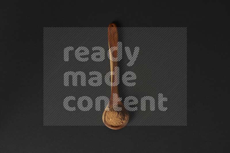 Cinnamon powder in a spoon ladle on black background