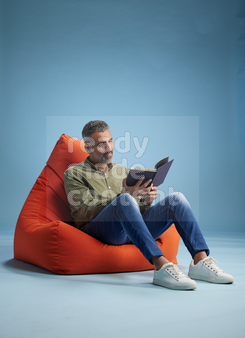 A man sitting on an orange beanbag and reading a book